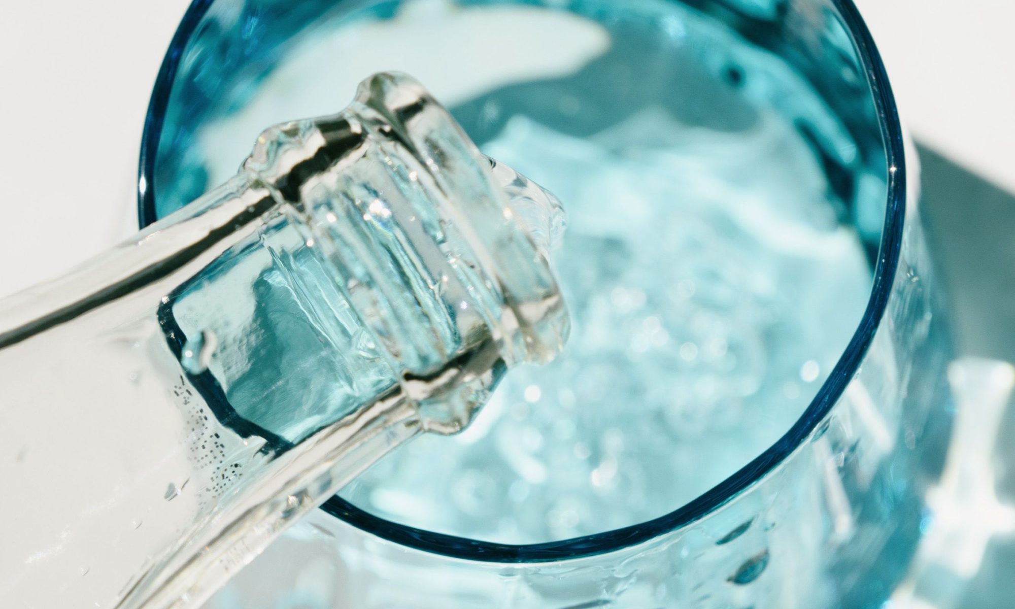 Close-up of water being poured into a blue glass in a sunny setting.